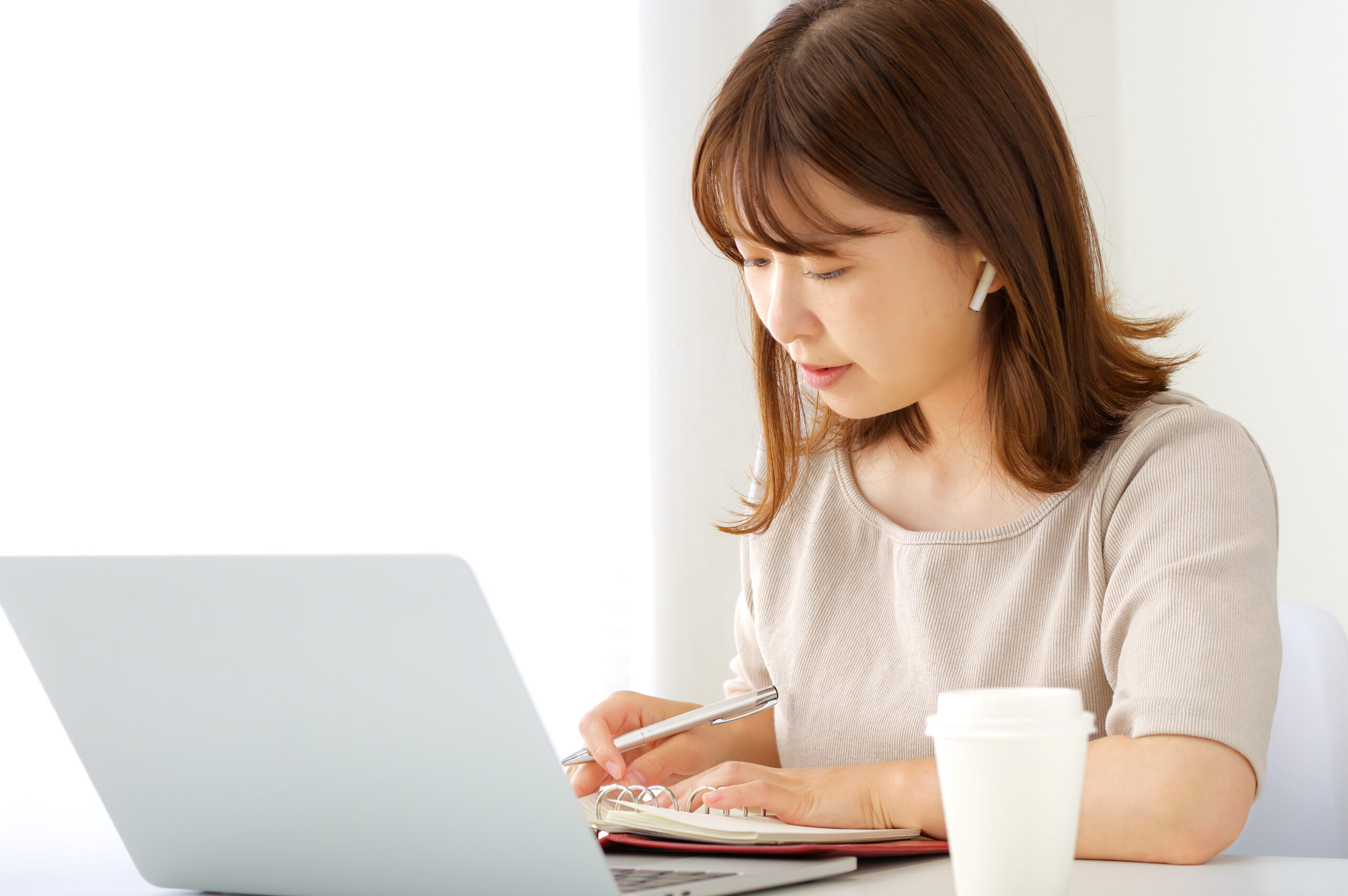 イヤホンを着けてパソコンでオンライン学習をする女性